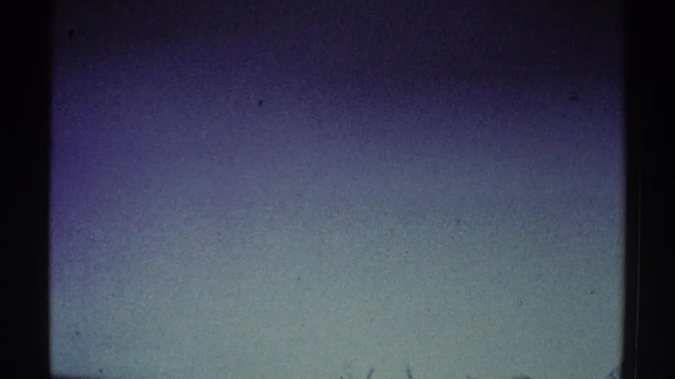1969 8mm Los Angeles footage opens on a dim, grainy wall area with soft blue-purple tones and dark frame edges.