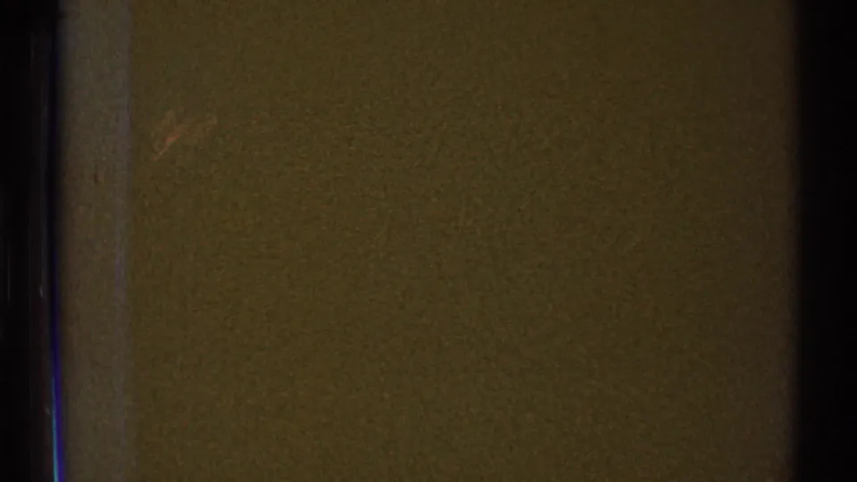 1969 home-movie frame showing a close, dim view of a doorway edge and brown interior wall in an empty apartment.