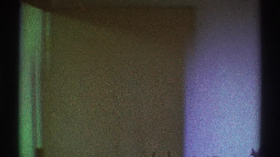 Grainy 1969 Los Angeles 8mm frame with an open doorway edge, greenish color shift, and pale wall surface beyond.
