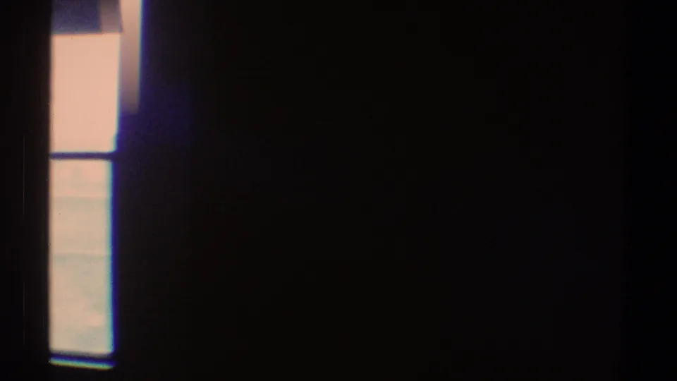1969 Los Angeles 8mm frame showing a narrow bright window area and deep shadow in an empty room.