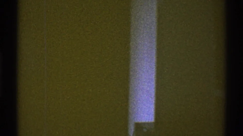 1969 Los Angeles interior frame with a dim wall, narrow bright vertical strip, and heavy film grain.