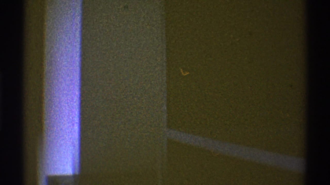 1969 Los Angeles 8mm frame showing a dim house interior, yellow wall, bright window edge, and heavy shadow.