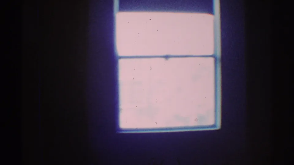 1969 Los Angeles 8mm view of a small bright window in a shadowed house interior with blue color shift.