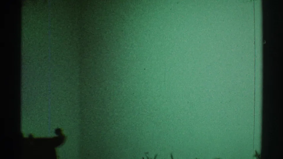 1969 Los Angeles 8mm frame with a green cast, dark vertical framing, and low furniture shapes in silhouette.