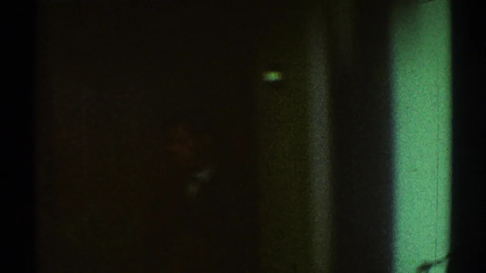 Very dark 1969 Los Angeles 8mm frame with a green-tinted edge and indistinct interior shapes.