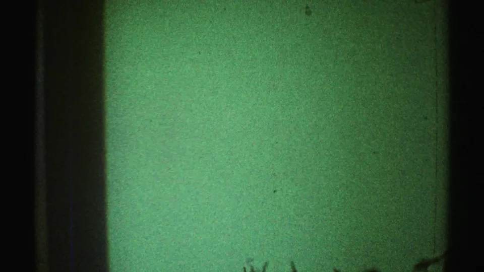1969 Los Angeles 8mm frame showing a green interior wall, dark vertical edges, visible grain, and faint lower-frame marks.