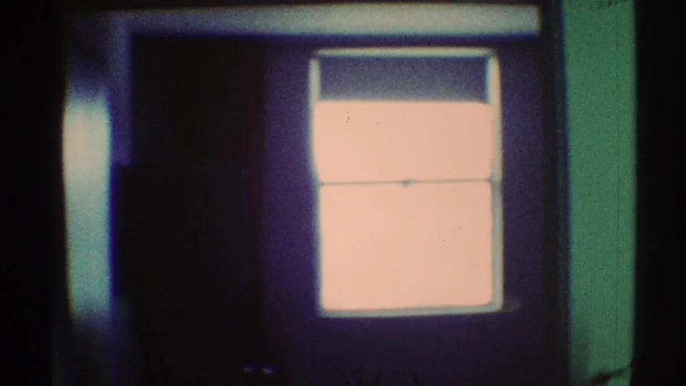 1969 Los Angeles 8mm frame showing a bright overexposed window within a dark green-tinted interior and shadowed furniture forms.