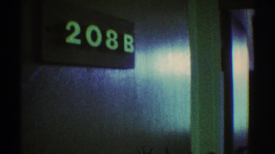 1969 Los Angeles 8mm frame with a green room-number sign reading 208B over a dark metallic hallway surface.