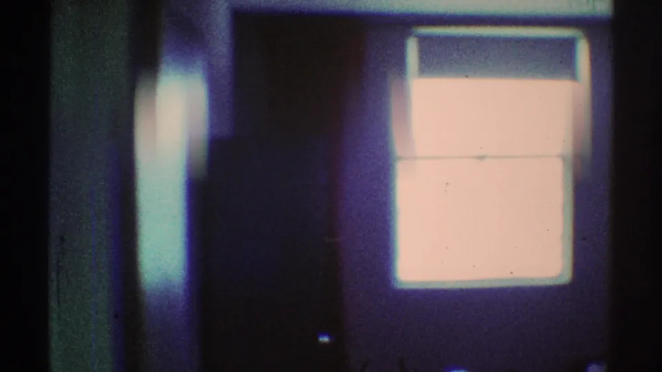 1969 Los Angeles 8mm frame showing a dark hallway area with a bright rectangular light source and soft handheld blur.
