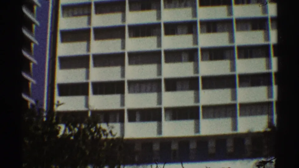 1969 Los Angeles home-movie view of a mid-century apartment exterior with balconies, tree tops, and a darker ground-level band.