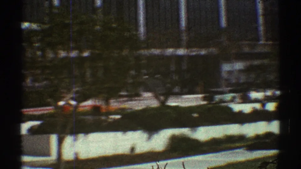 1969 Los Angeles frame with landscaped roadside planting, trees, and a tall columned building partly obscured by motion blur.