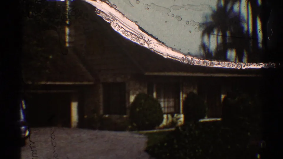 A house exterior appears beside the Los Angeles street, partly obscured by 8mm film marks and dark roadside trees.