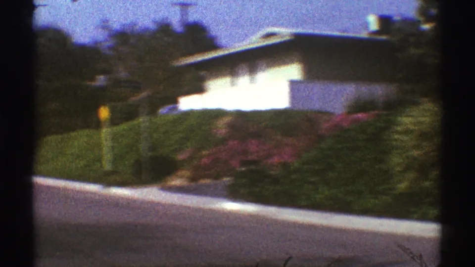 1969 Los Angeles residential view with a low house, trimmed hedges, sloping street, and garden plantings.