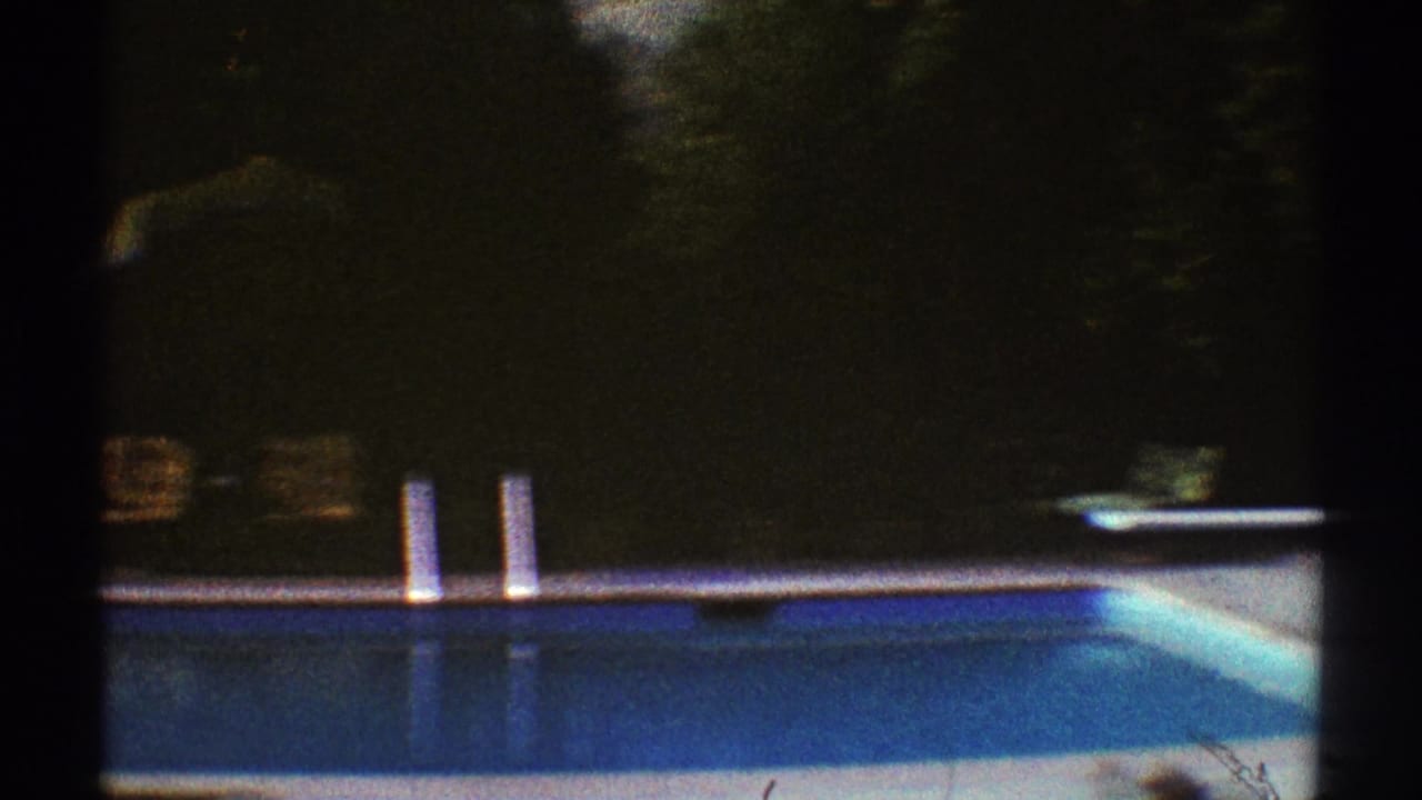 Backyard swimming pool with diving board, lounge chairs, trees, and dark film edge.