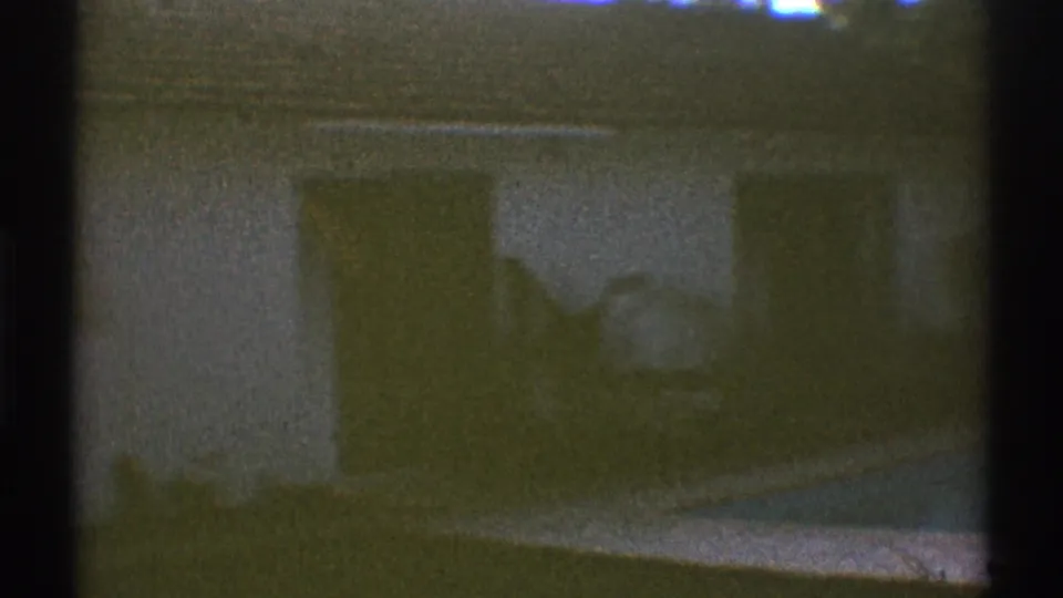 1969 Los Angeles home-movie frame showing part of a house beyond the pool, with a large window, yard, and soft exposure.