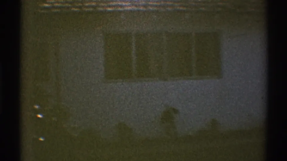 1969 Los Angeles backyard frame with a house wall and broad window behind the pool, partly obscured by grain and low exposure.