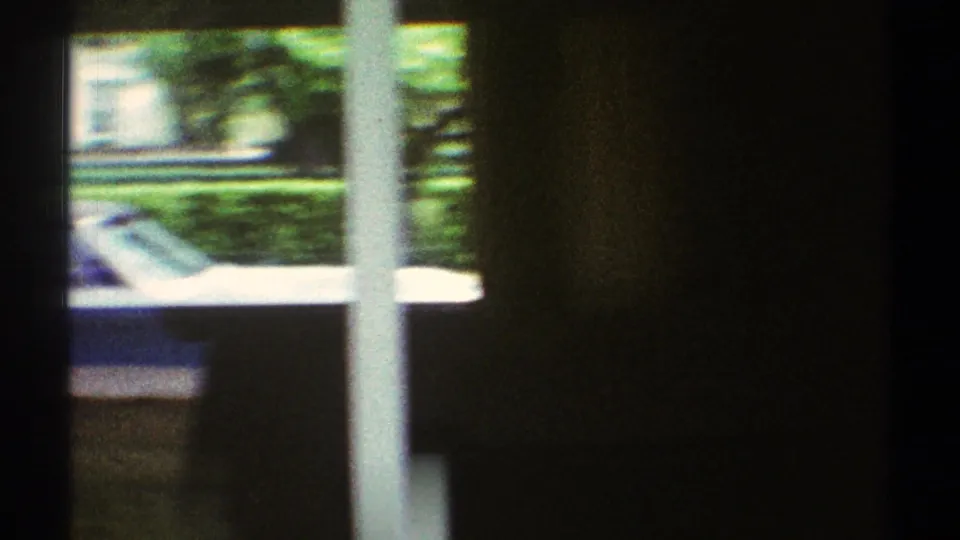 1969 Los Angeles interior frame looking through a window toward green landscaping and a partial car outside the private house.