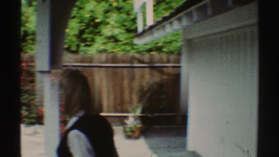 1969 Los Angeles backyard view showing a white garage or exterior wall, wooden fence, hedges, patio ground, and plants.