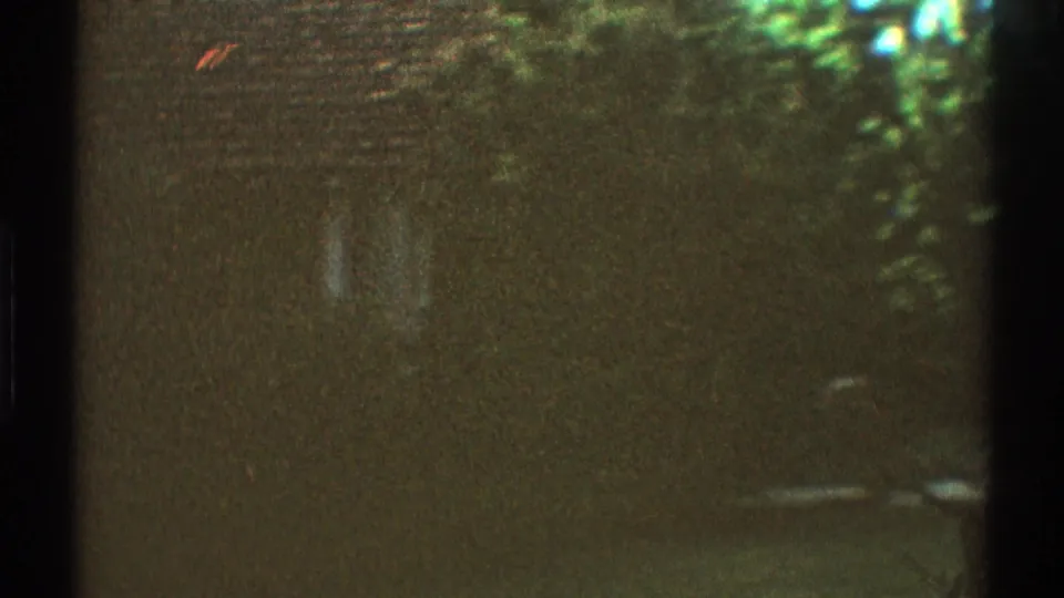 Dark 8mm frame from the 1969 Los Angeles clip, with only faint outlines of foliage and street features visible through heavy exposure loss.