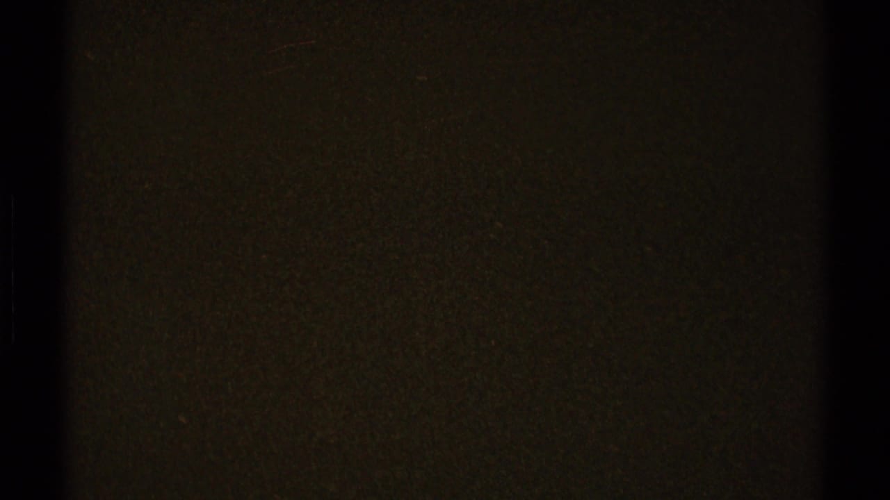 Dark grainy film frame with faint olive tone and vertical black edge.