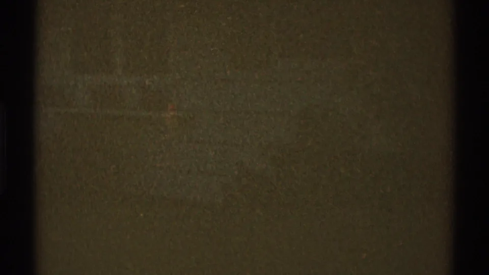 Low-exposure archival frame showing a dark textured surface, faint horizontal forms, and visible 8mm grain.