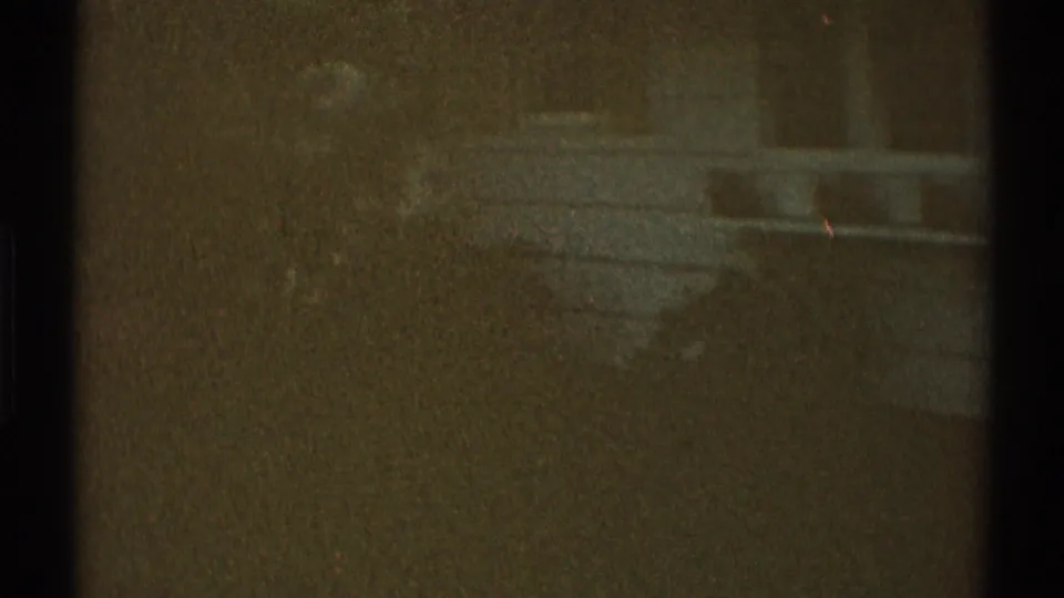 Late-1960s 8mm frame, based on metadata, with dark green-brown tones, faint pale shapes, and visible dust specks.
