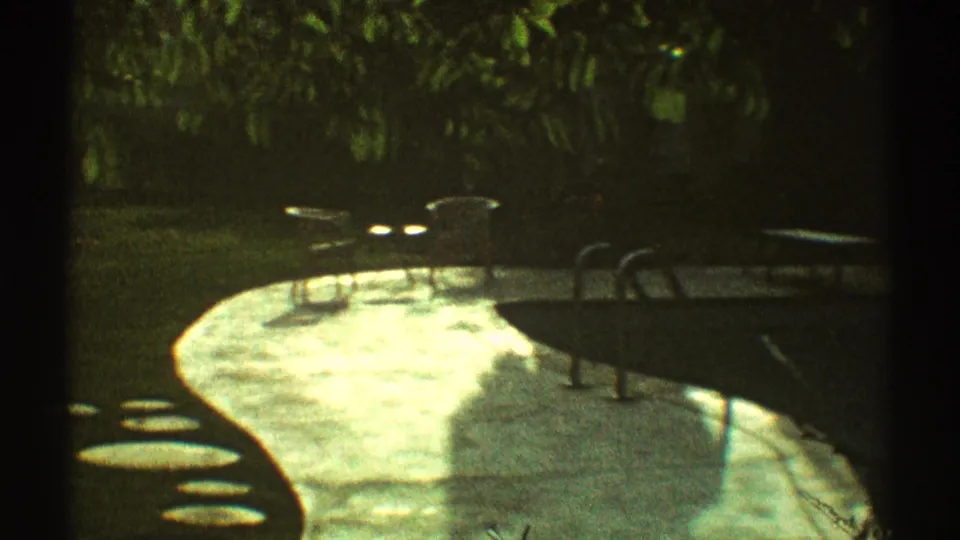 1969 Los Angeles backyard pool area with a curved concrete deck, small patio tables, chairs, and dense greenery.
