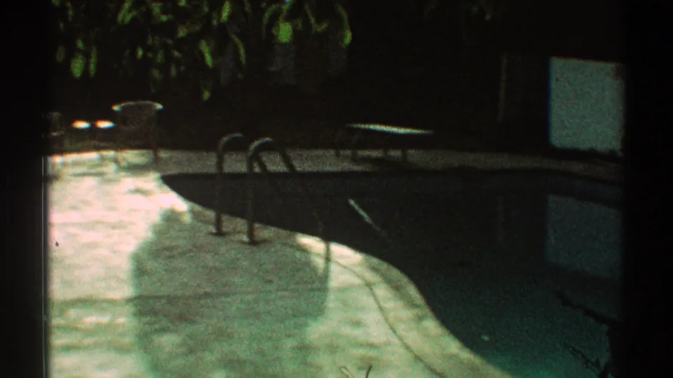 1969 Los Angeles home-movie view of a backyard swimming pool with metal ladder, lounge chair, concrete patio, and greenery.