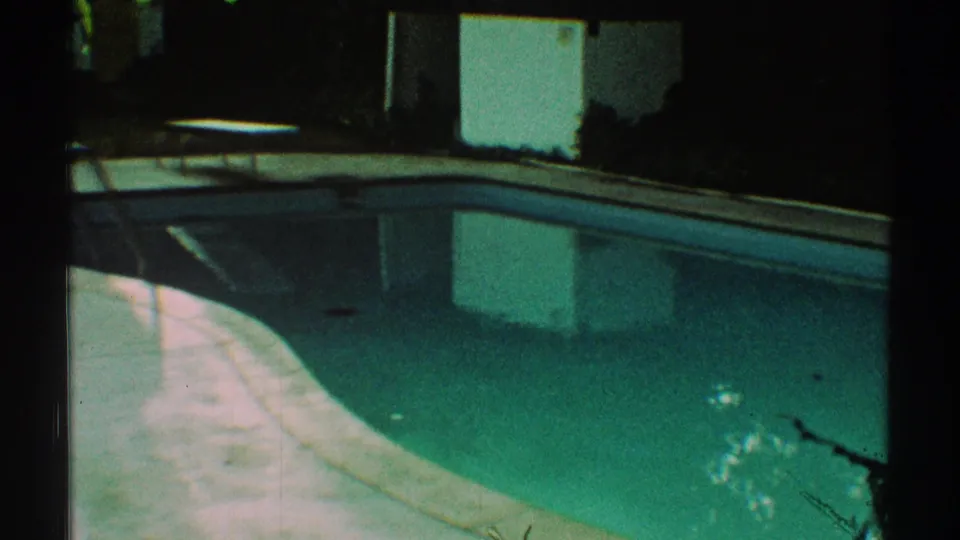 1969 Los Angeles backyard pool frame showing turquoise water, a curved concrete border, shaded patio, and nearby wall or structure.