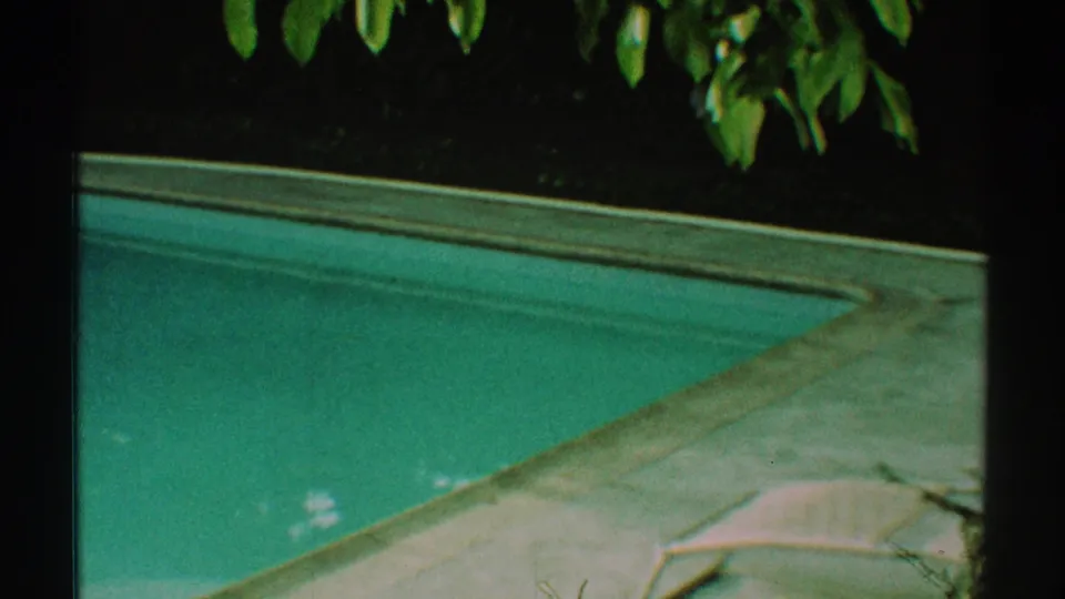 1969 Los Angeles home-movie view of a backyard pool corner, showing turquoise water, pale deck surface, and leafy branches overhead.