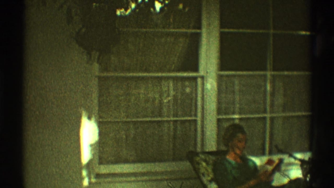 Woman seated on a porch chair reading beside a large window with curtains.