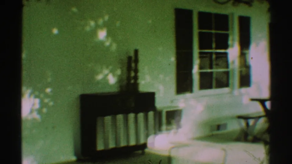 The camera pans across a Los Angeles residential porch with white siding, windows, shutters, a dark cabinet or screen, and sunlit steps.