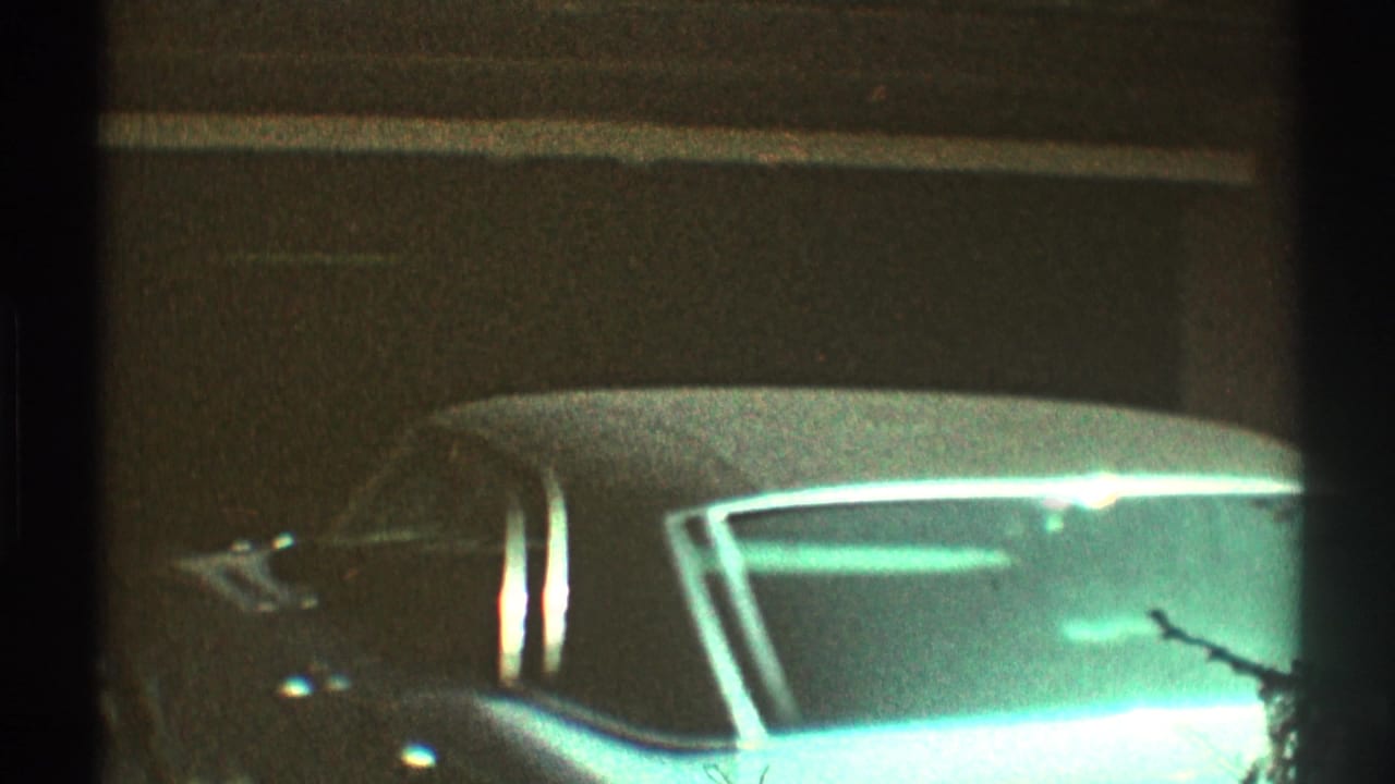 1969 Los Angeles 8mm frame showing a light-colored vintage car with chrome trim near a dark garage opening.