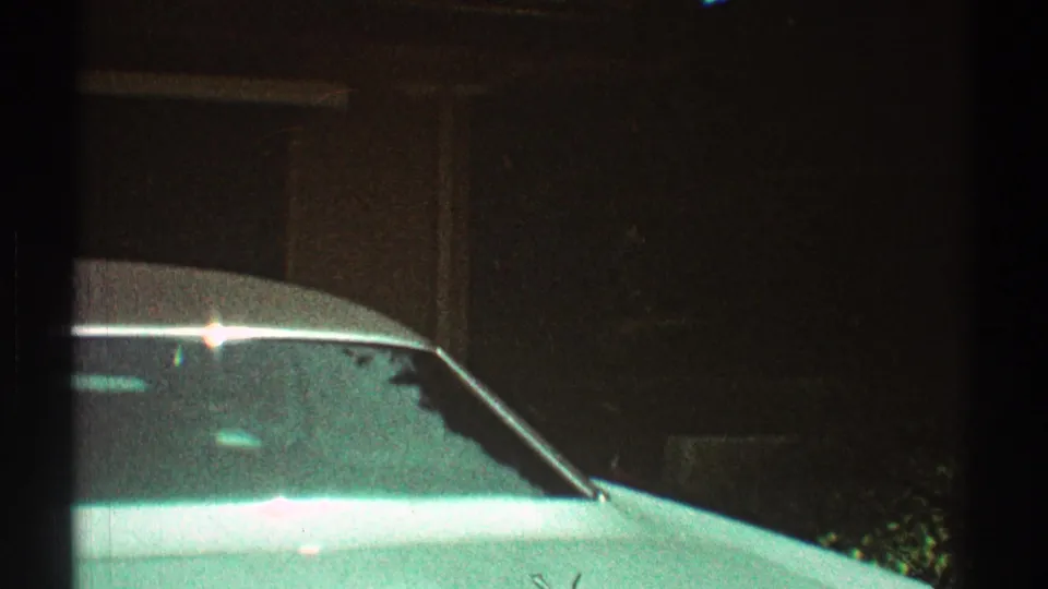1969 Los Angeles home-movie frame with the front of a light-colored vintage car partly blocked by dark foreground framing.