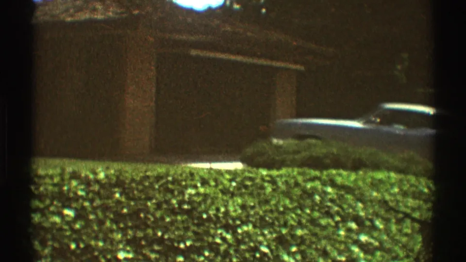 1969 Los Angeles residential exterior with garage doors, hedges, lawn, and a partly visible parked car.