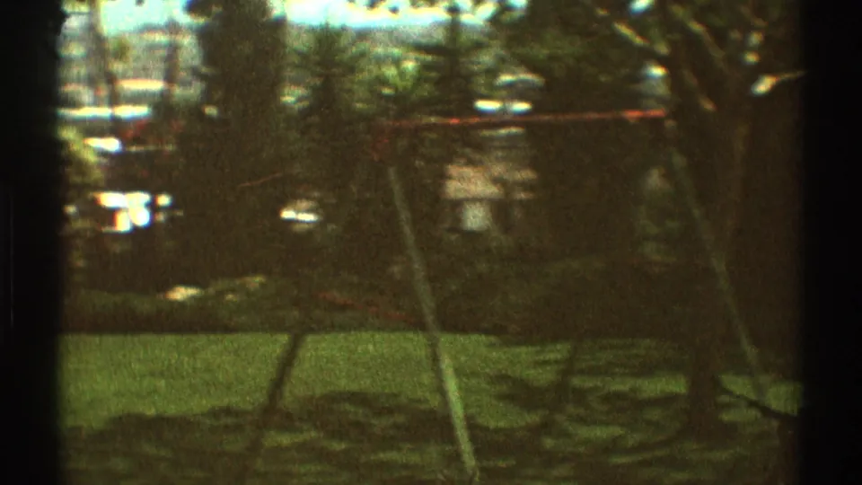 1969 Los Angeles backyard scene with a metal swing set, shaded grass, hedges, trees, and distant rooftops.