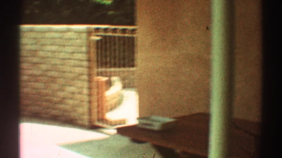 1969 Los Angeles backyard patio corner with a wood fence, small gate or railing, light chair, and stucco wall edge.