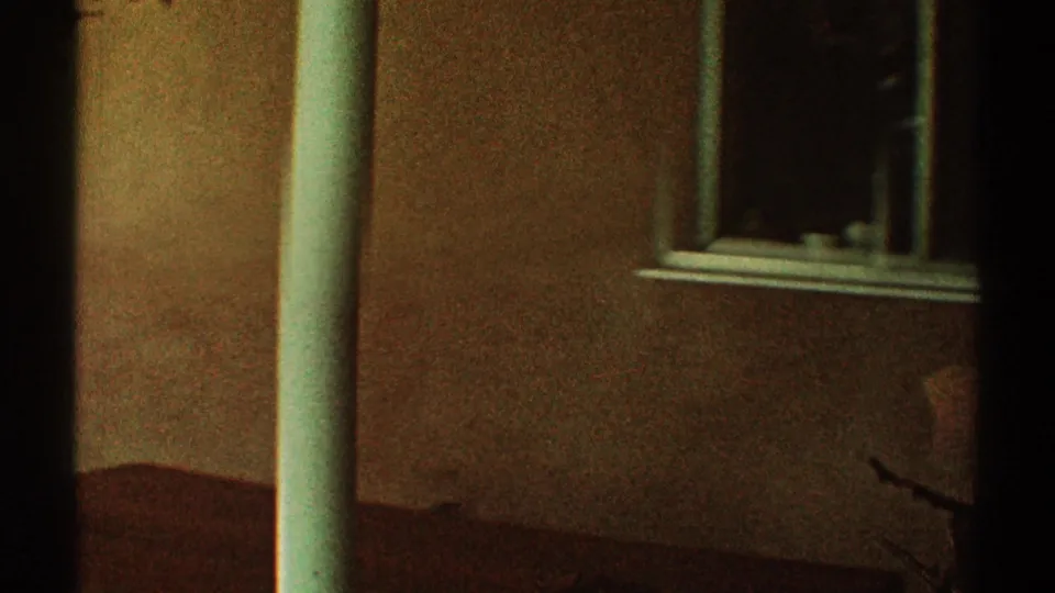 1969 Los Angeles 8mm frame showing a dim stucco house exterior, white post, dark doorway, and window in low light.