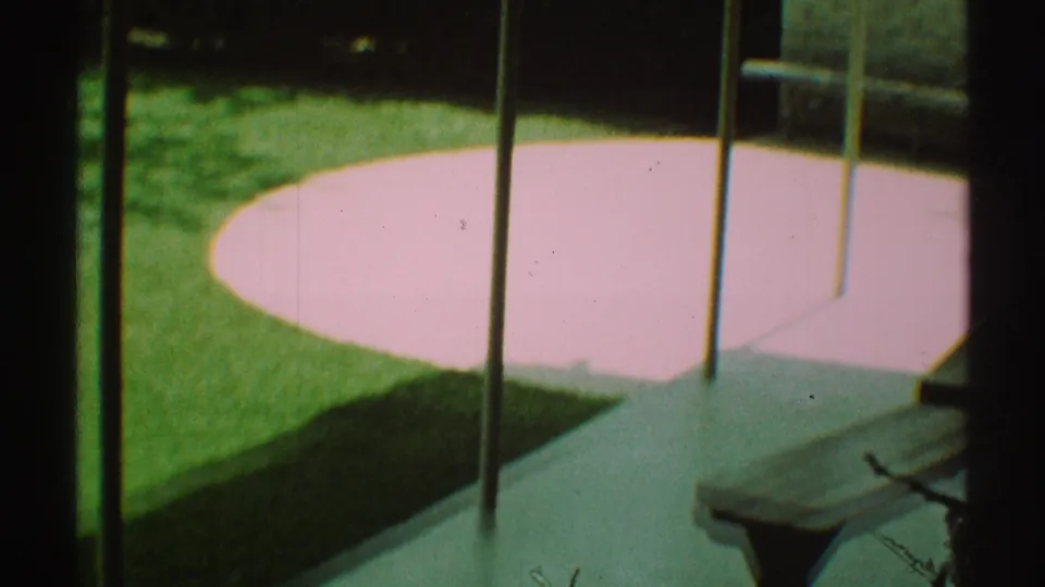 1969 Los Angeles backyard frame showing lawn, concrete patio, vertical rail-like lines, and a pale pink circular feature in sunlight.