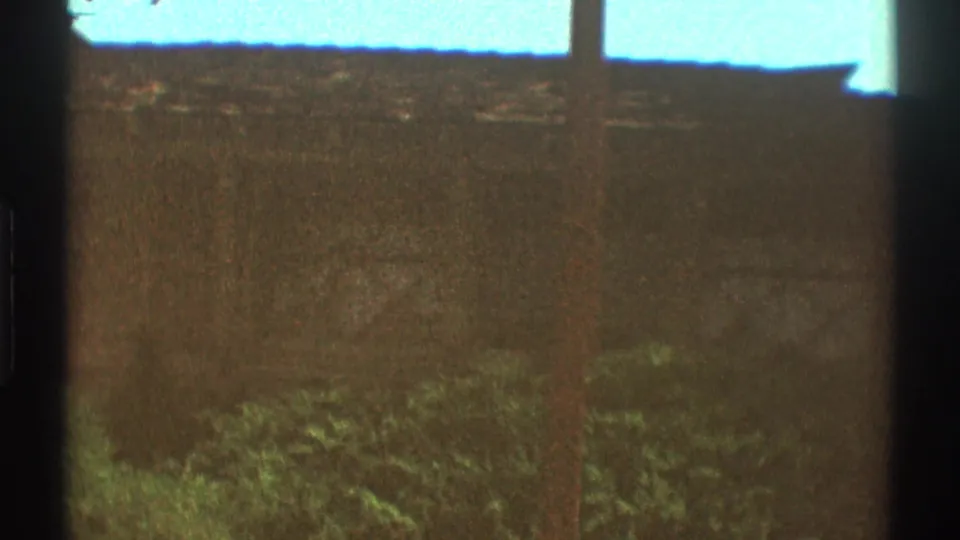 1969 Los Angeles home-movie frame with a roofline, vertical utility pole, chimney, shrubs, and blue sky.