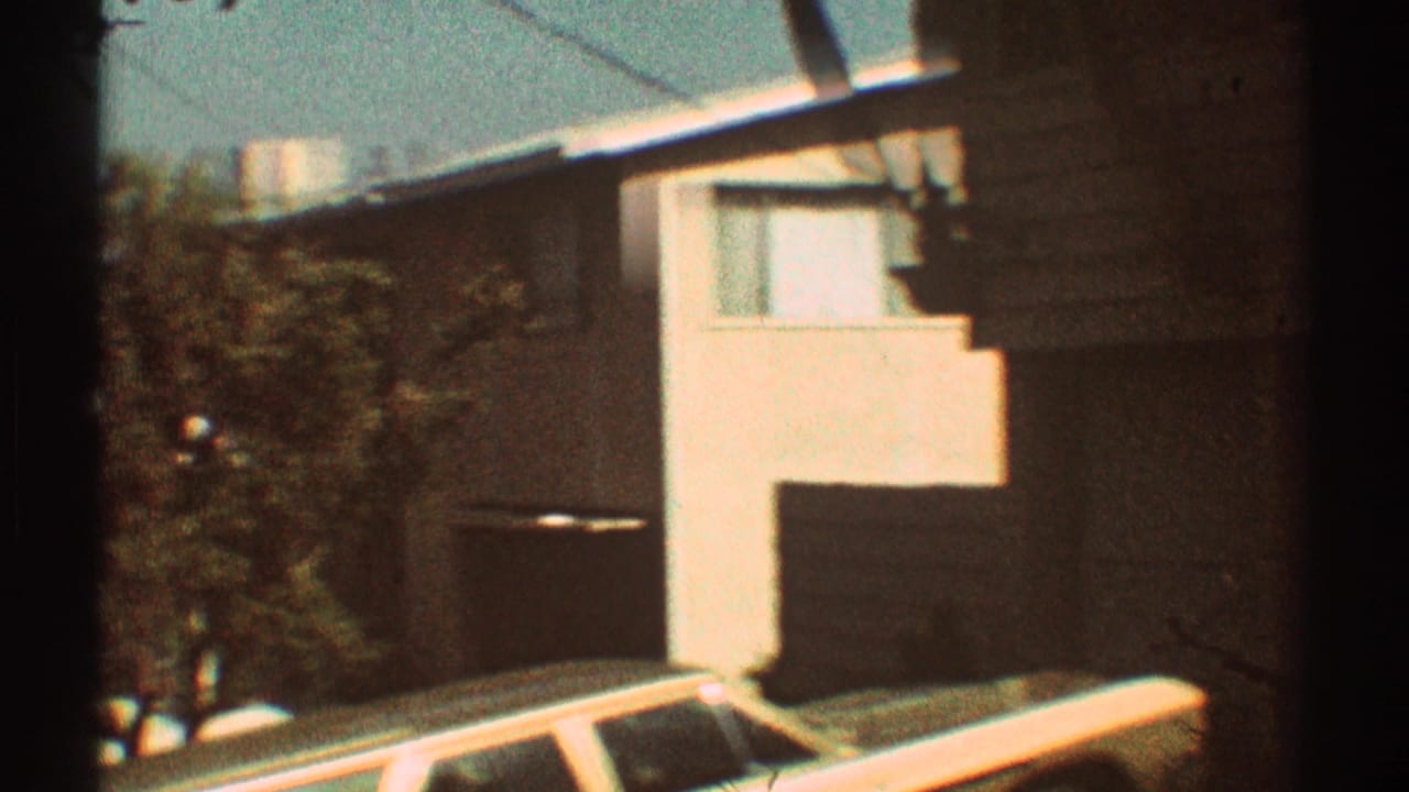 Tan building beside a parked white car on a sunny residential street.