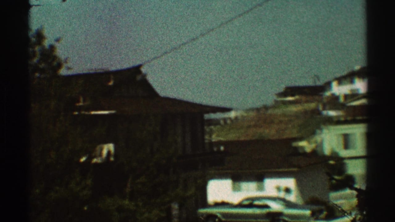 Dark-edged 8mm frame of houses, trees, utility wire, and a parked car in a residential area.