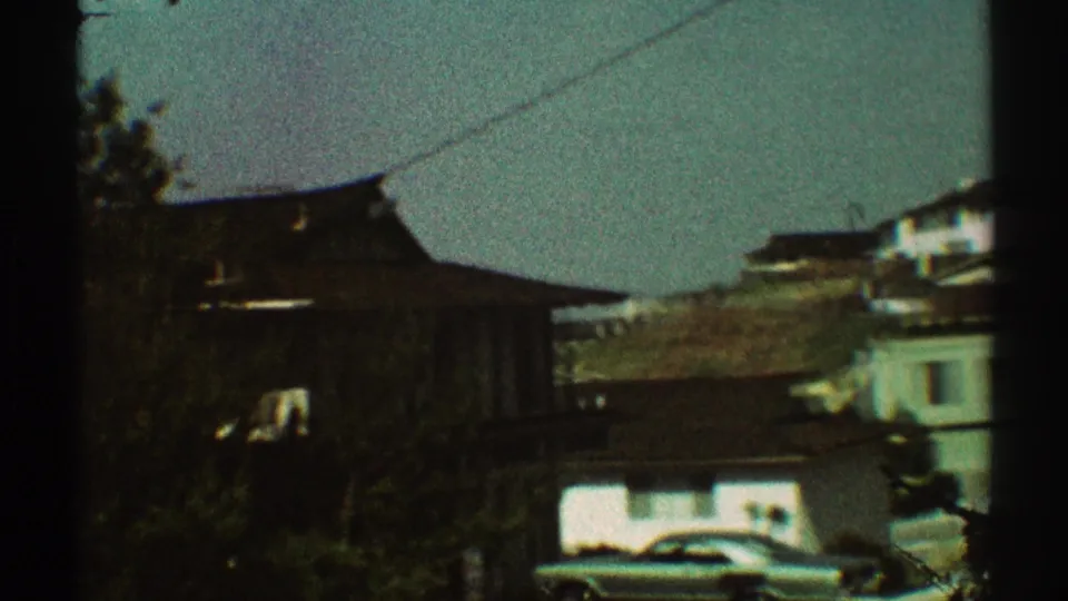1969 Los Angeles home-movie frame showing rooftops, trees, a parked car, and overhead wire during a handheld neighborhood pan.