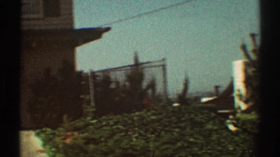 1969 Los Angeles residential exterior with a house edge, hedge, fence, overhead wires, and soft faded 8mm color.
