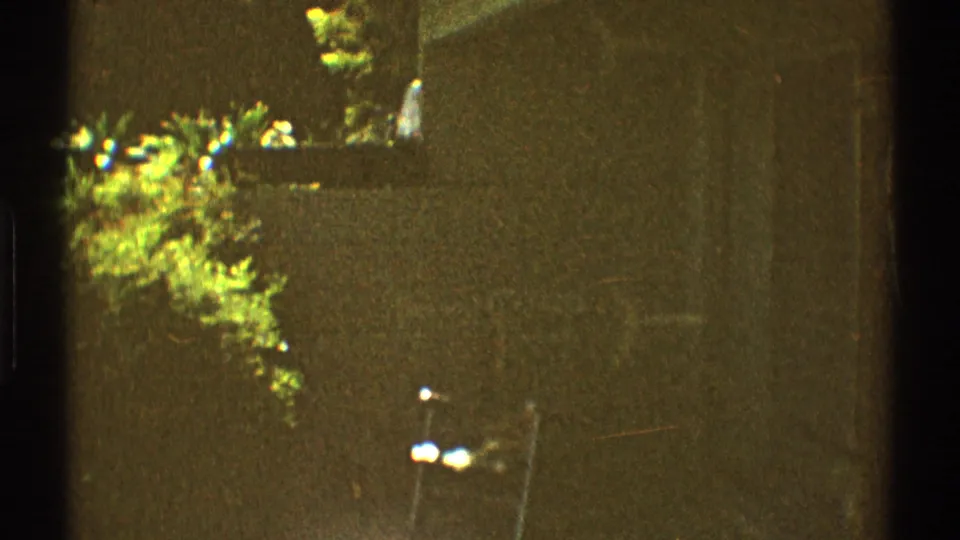 1969 Los Angeles 8mm frame showing a patio edge with a brick wall, metal chair, garden foliage, and irregular sunlight.