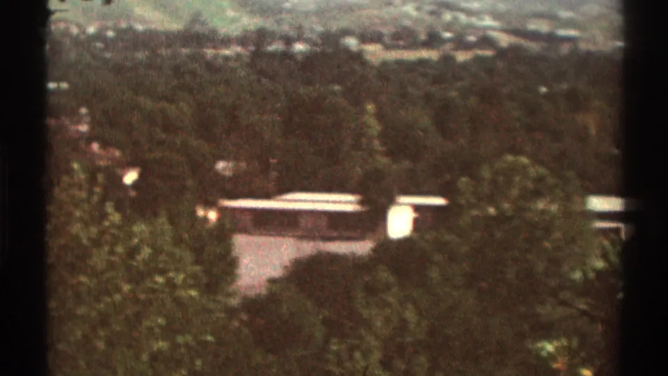 Close 1969 Los Angeles-area home-movie view of a flat-roof house partly obscured by trees and hillside vegetation.
