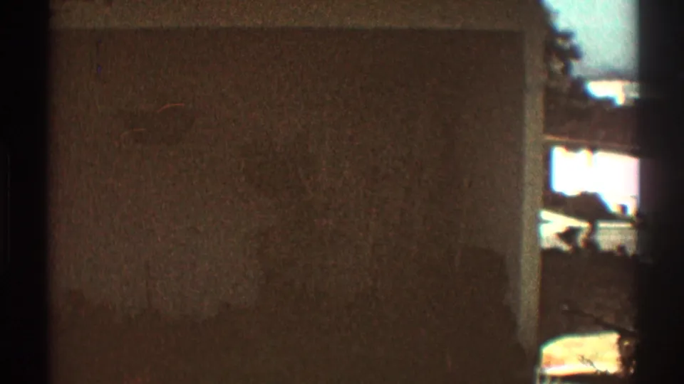 Soft 8mm frame from the Los Angeles residential scene, centered on a plain exterior surface with heavy dark borders and bright edge exposure.
