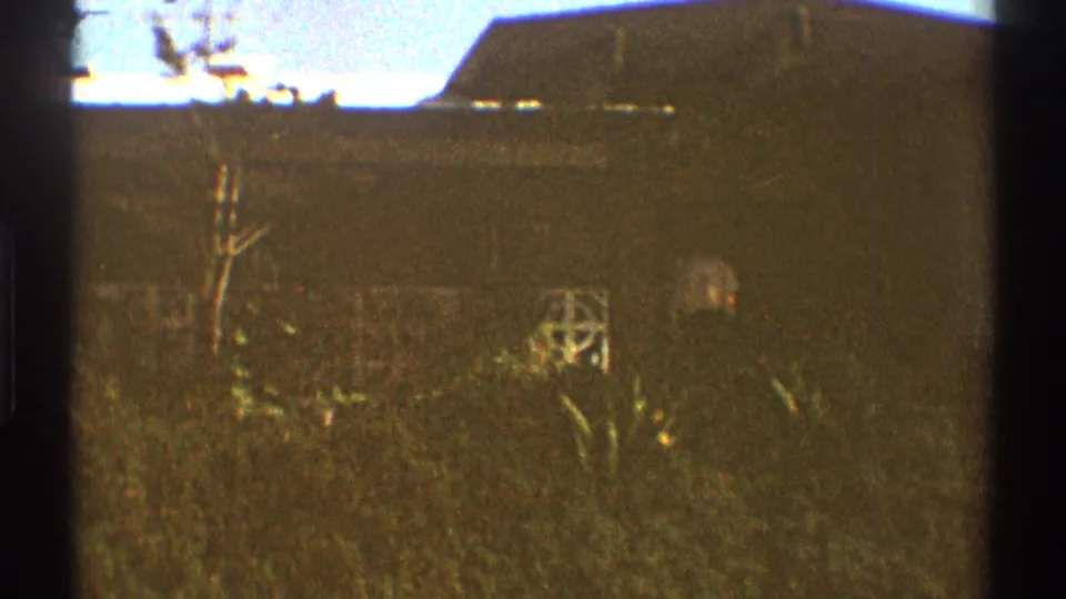 A low Los Angeles residential exterior and yard planting appear in a soft, grainy 1969 8mm frame.