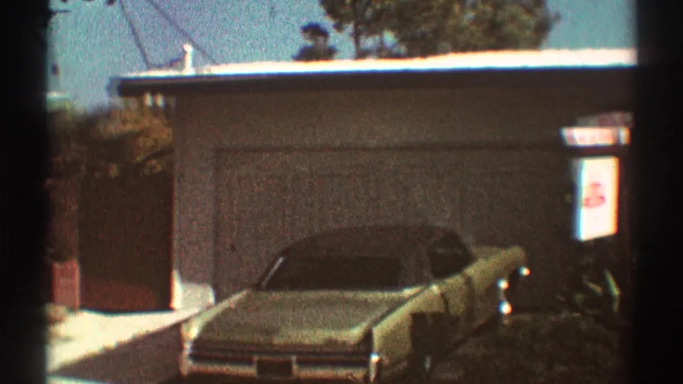 A vintage car sits in a residential driveway outside a low Los Angeles house in 1969 home-movie footage.