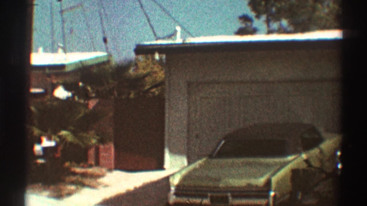 Driveway car in front of a single-car garage on a sunny residential street.
